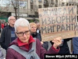 Një protestuese mban në dorë një pankartë me mbishkrimin: “Rrofshin emigrantët zgjedhorë!”