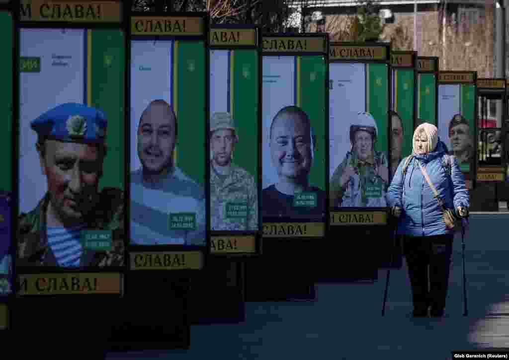 O femeie trece pe lângă panourile din Bucea pe care se află chipurile soldaților ucraineni care au murit pentru a-și apăra țara.