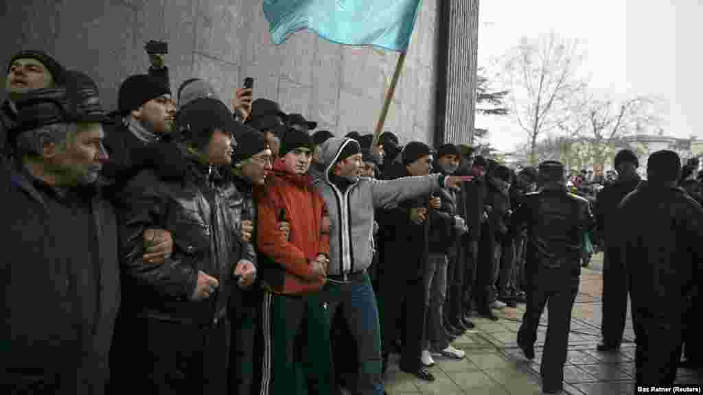 Krími tatárok a zászlójukkal a krími parlamentnél tartott tüntetésen Szimferopolban 2014. február 26-án. Egy héttel korábban egy krími politikus felvetette a félsziget Ukrajnától való elszakadásának lehetőségét. A kijevi tüntetők akkoriban éppen azon voltak, hogy kiszorítsák a hatalomból Viktor Janukovics oroszbarát elnököt, amit az ukránok „a méltóság forradalmának” neveztek el
