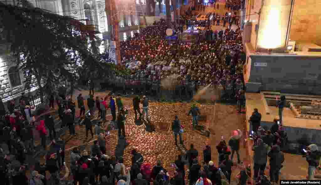 Un cordon de polițiști față în față cu protestatarii pe o stradă care duce la intrarea din spate a clădirii parlamentului georgian (în dreapta).