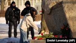 Police officers watch a woman laying flowers in tribute to Aleksei Navalny at a monument in St. Petersburg on February 18. Almost 200 people have been arrested in the city in the past week for attending memorials for the opposition activist, who died in prison on February 16.