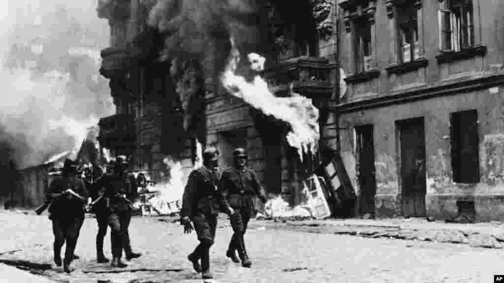 След потушаването на въстанието на 16 май 1943 г. нацистките войници взривяват синагогата. Този кадър е уловил как нацистки офицери се разхождат по улиците, докато сгради във Варшавското гето горят. 