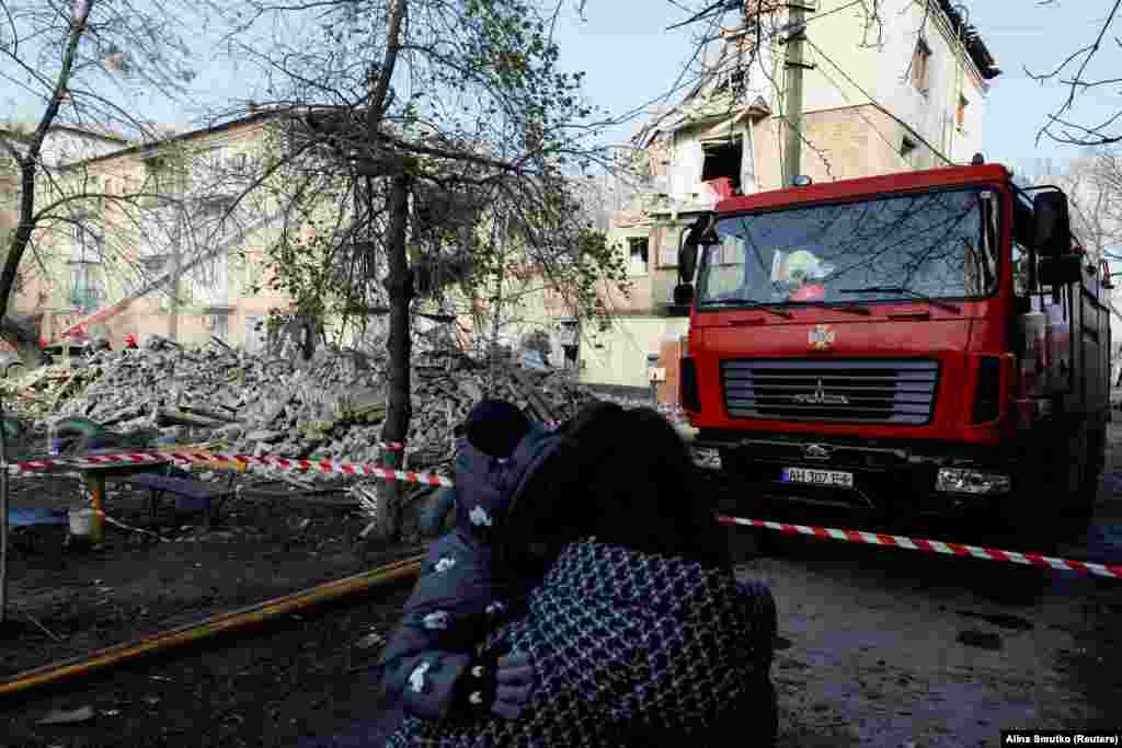 Жінка з дитиною дивляться на пошкоджений житловий будинок. У повідомленні, розміщеному в телеграмі, Офіс генерального прокурора України заявив, що російські війська застосували зенітно-ракетний комплекс С-300, випустивши чотири ракети по місту, які влучили в чотириповерховий житловий будинок.