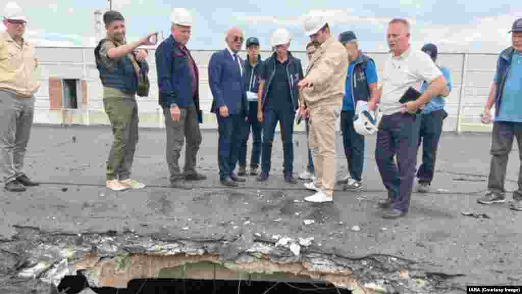 A Nemzetközi Atomenergia-ügynökség ellenőrei, köztük Rafael Grossi, a NAÜ vezetője (jobbra középen kék mellényben) egy nukleáris üzemanyagot tároló épületre csapódott gránát okozta sérüléseket vizsgálnak 2022 szeptemberében. Grossi és Putyin idei, március 6-i zárt ajtós találkozójának részletei nem világosak, a NAÜ vezetője csupán egy „fontos eszmecserét” jelentett be az atomerőművel kapcsolatban