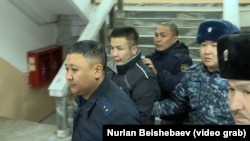 Укук коргоо органдарынын кызматкерлери Азамат Эстебесовду алып баратышат. 