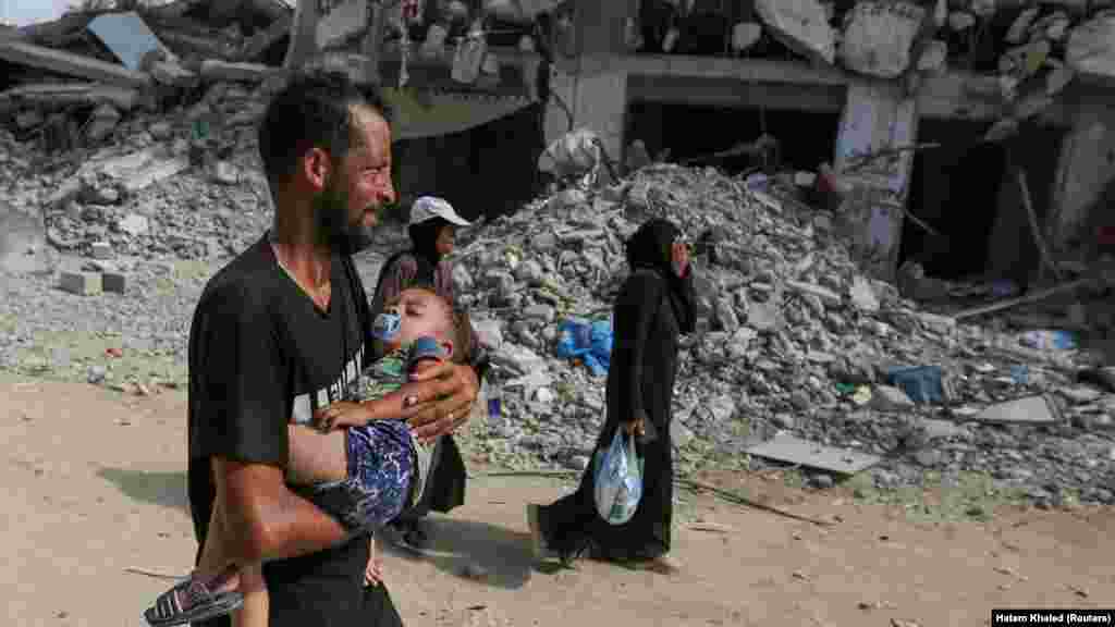 Një burrë palestinez bart një fëmijë, ndërsa ecën për t'u kthyer në pjesën lindore të Han Junisit pasi forcat izraelite u tërhoqën nga zona pas një bastisjeje, në mes të konfliktit Izrael-Hamas, në Han Junis, në jug të Rripit të Gazës më 30 korrik 2024. 