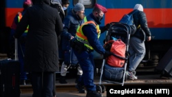Egy, az orosz–ukrán háború elől menekülő nő babakocsiját rakja a peronra egy rendőr a záhonyi vasútállomáson 2022. március 1-jén