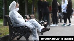 A woman in a face mask and protective suit sits on a bench in central Moscow.
