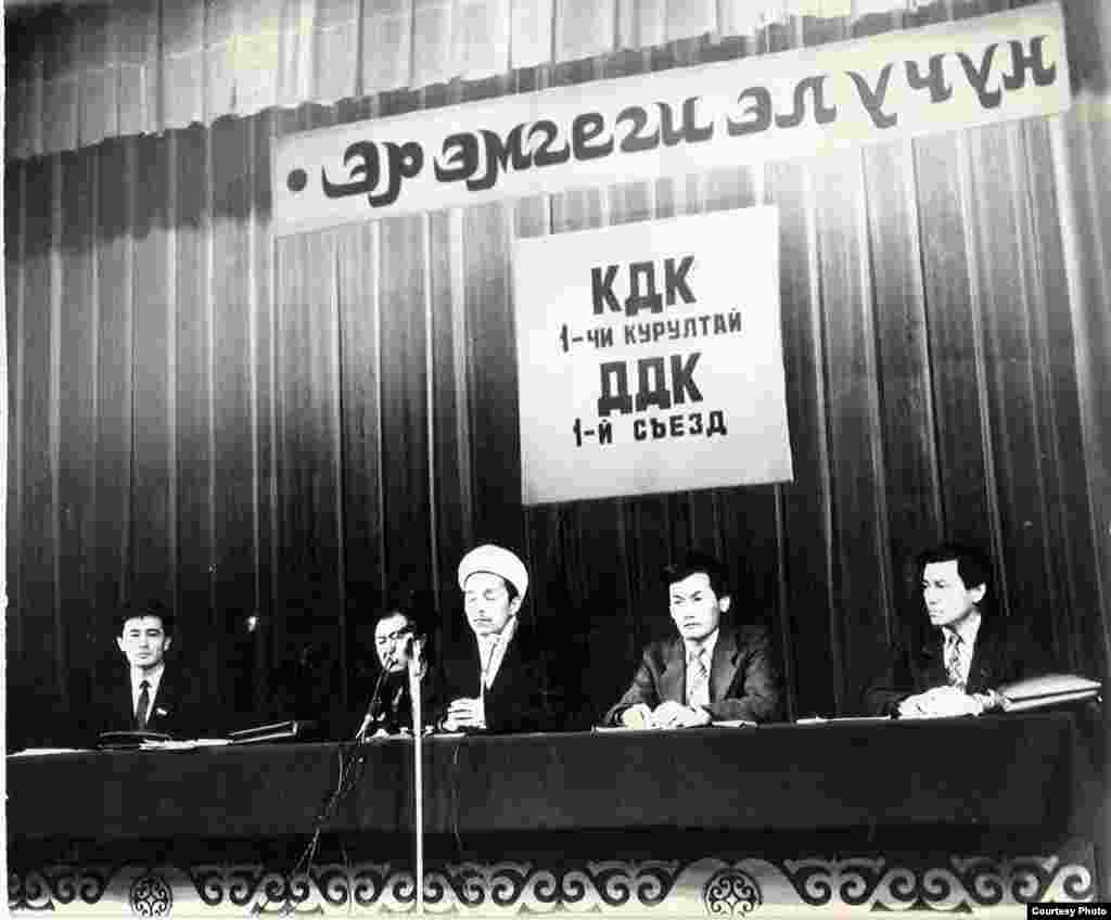 Открытие съезда Демократического Движения "Кыргызстан" (КДК) в г.Бишкек. 09.2.1991. - Торжественное открытие I съезда Демократического Движения "Кыргызстан" (КДК) 9 февраля 1991 г. В президиуме сидят депутат Омурбек Текебаев, депутат и писатель, со-председатель КДК Казат Акматов, секретарь Муфтията Кыргызстана Дуйшонбек Отонбай уулу, политики и со-председатели КДК Кадыр Матказиев и Джыпар Джекше (слева направо). КДК было объединением ряда антикоммунистических реформаторских партий, движений и неправительственных организаций Кыргызстана. Оно было создано на Учредительной конференции 25-26 мая 1990 г., и через 9 месяцев (9-10 февраля 1991 г.) состоялся Первый курултай (съезд) КДК в г. Бишкек.