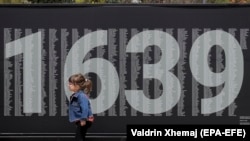 Një vajzë e vogël kalon pranë një bilbordi ku janë shkruar emrat e personave të pagjetur që nga lufta e fundit në Kosovë. Prishtinë, 29 prill 2021. 