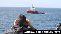 Жээкте дүрбү салып турган Британиянын кылмыштуулукка каршы агенттигинин кызматкери Иллюстрациялык сүрөт.