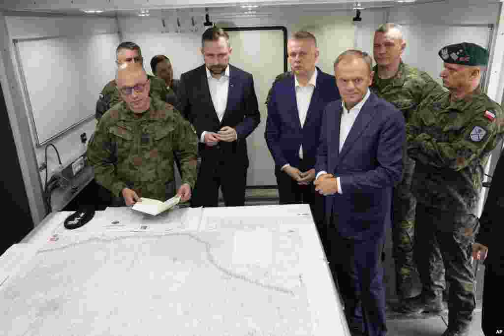 Premierul polonez Donald Tusk (în față, dreapta), ministrul Apărării Wladyslaw Kosiniak-Kamysz (centru) și ministrul de Interne Tomasz Siemoniak (centru dreapta) vizitează soldații polonezi la Dubicze Cerkiewna, în estul țării, la 29 mai. „Nu avem de-a face doar cu azilanți, avem de-a face cu o operațiune coordonată, foarte eficientă - în multe privințe - de a penetra granița poloneză și de a destabiliza țara”, a spus Tusk. 