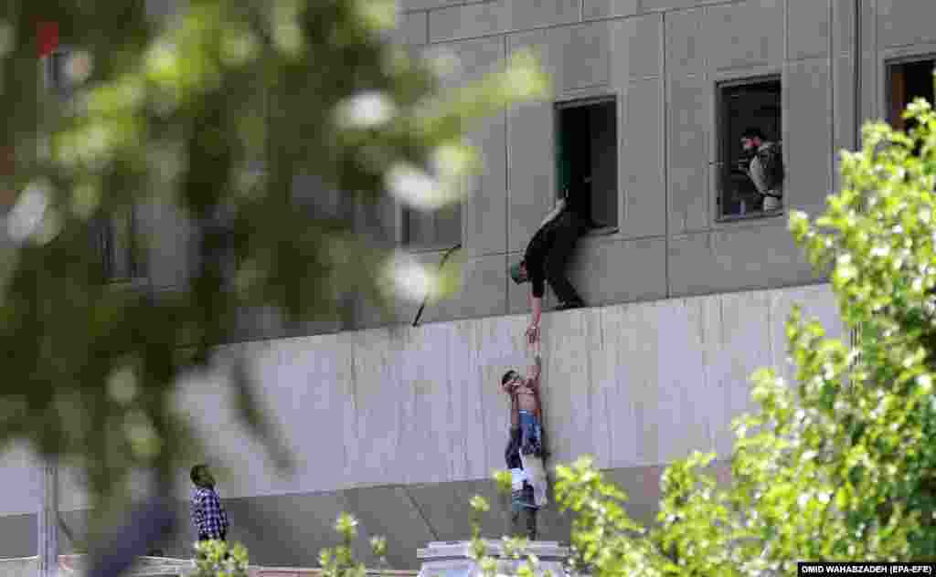 Iranski policajac pomaže civilima da napuste zgradu parlamenta u Teheranu. najmanje 12 ljudi je ubijeno u dva napada 7. juna u teheranu - na zgradu parlamenta i grobnicu vrhovnog verskog vođe Ajatolaha Homeinija. (EPA-EFE/Omid Wahabzadeh)