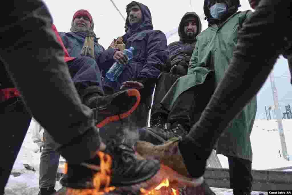 Refugiații se încălzesc la un foc improvizat sub cerul liber.