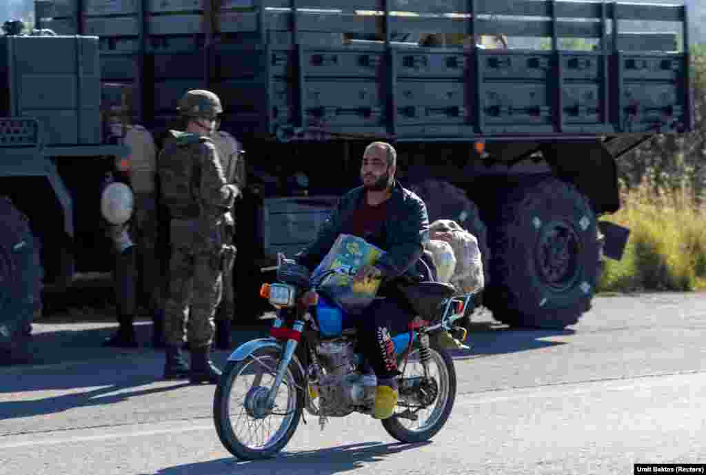 Një banor vendas kalon pranë një autokolone ruse pranë bazës ajrore Hmeimim. "Vendasit vetëm po shikojnë", thotë Bektas për situatën rreth bazës, e cila tani është pa mbrojtje të jashtme ushtarake përgjatë perimetrit të saj. "Ka shumë dyqane me alfabetin rus në to në fshatin afër bazës ajrore", tregon Bektas, por të gjitha tani janë mbyllur. "Nuk ka asnjë ushtar rus që del vetëm ose me makinë jo të blinduar apo diçka të tillë".
