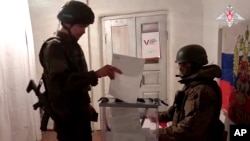 Зображення з відео, яке опублікувала пресслужба Міноборони Росії в середу, 13 березня 2024. Російський військовослужбовець віддає свій бюлетень під час незаконного голосування на виборах президента Росії в окупованій частині Донецької області
