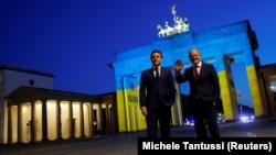 Președintele francez Emmanuel Macron și cancelarul german Olaf Scholz la Poarta Brandenburg de la Berlin luminată în culorile drapelului ucrainean, 9 iunie 2022.