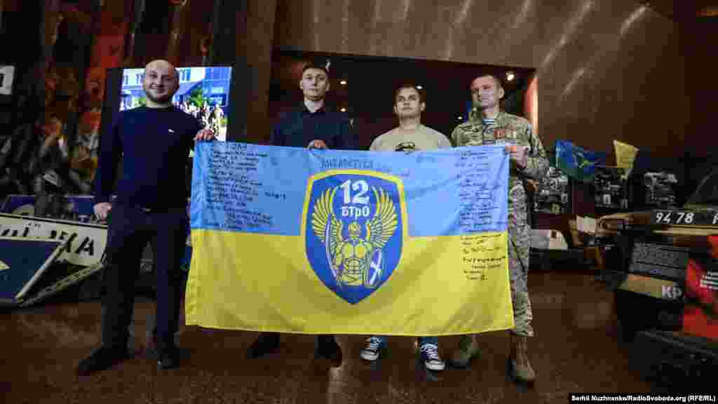 Бійці 12-го батальйону територіальної оборони «Київ» зі своїм прапором. Зліва направо: Олександр Полудень, метеоролог та командир відділення, сержант В’ячеслав Цветінський, боєць підрозділу Ілля Костін, В’ячеслав Назаренко, командир 3-го взводу 1-ї роти охорони 12-го БТрО «Київ».