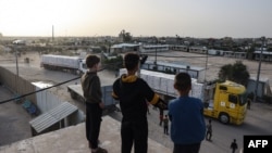 Copii și tineri urmăresc intrarea camioanelor cu ajutoare prin punctul de trecere a frontierei Rafah. 26 noiembrie, 2023
