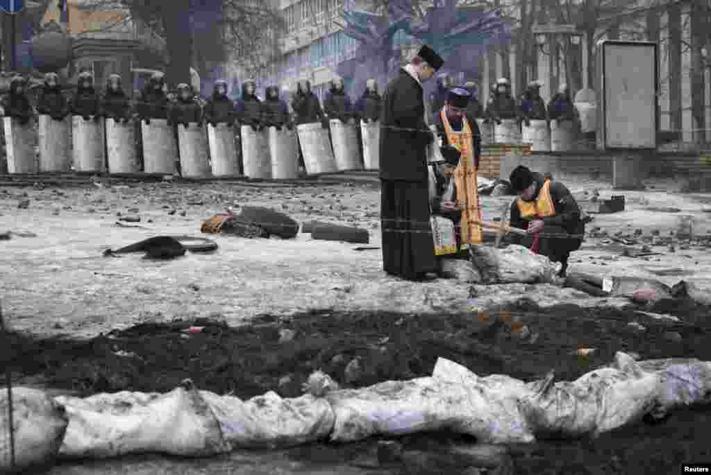 Священики запалюють свічки під час служби на місці недавніх зіткнень біля барикад на Грушевського, Київ, 13 лютого 2014 року
