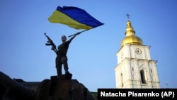 A woman waves a Ukrainian flag atop a destroyed Russian tank that was part of an open-air exhibition of destroyed military equipment and weapons of the Russian Army on Mykhailivska Square in Kyiv on June 17.