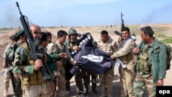 Kurdish Peshmerga soldiers pose with a flag belonging to Islamic State after they regained control of an area west of Kirkuk in Iraq from the Islamist extremists earlier this year. 