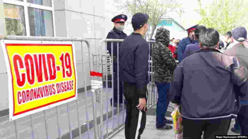 COVID-19 деген жазуы бар баннердің жанында тұрған халық. 6 сәуір 2020 жыл. 