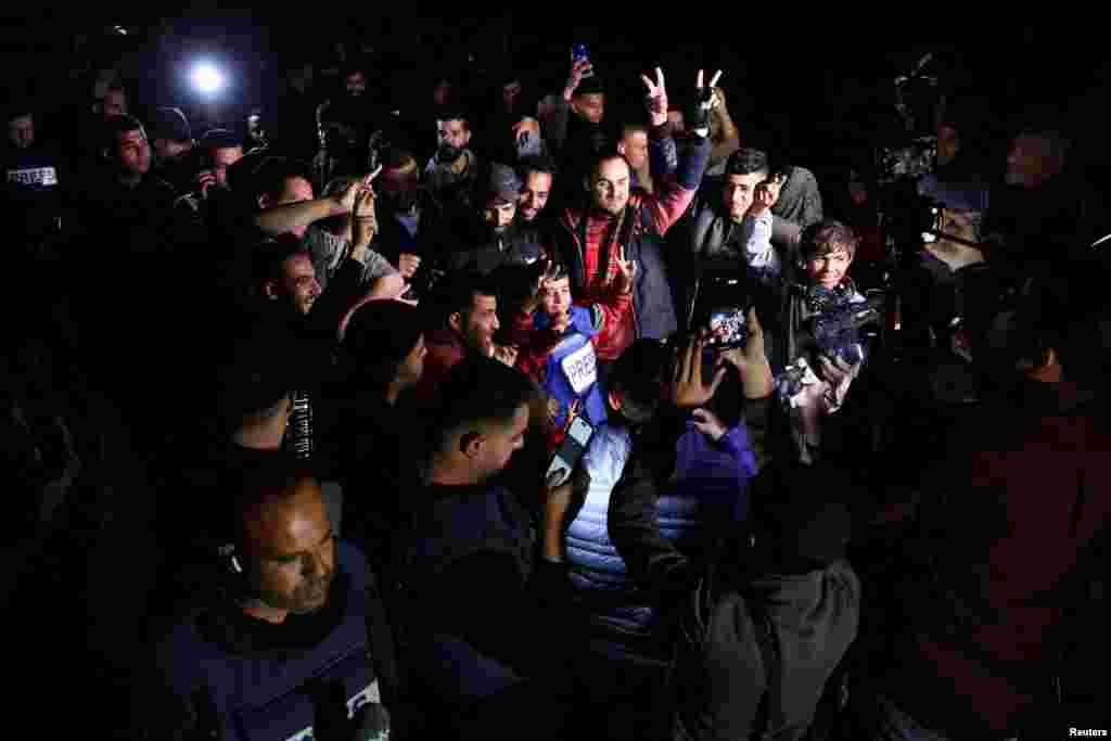 Punonjës të mediave shihen duke raportuar derisa palestinezët festojnë arritjen e armëpushimit. 