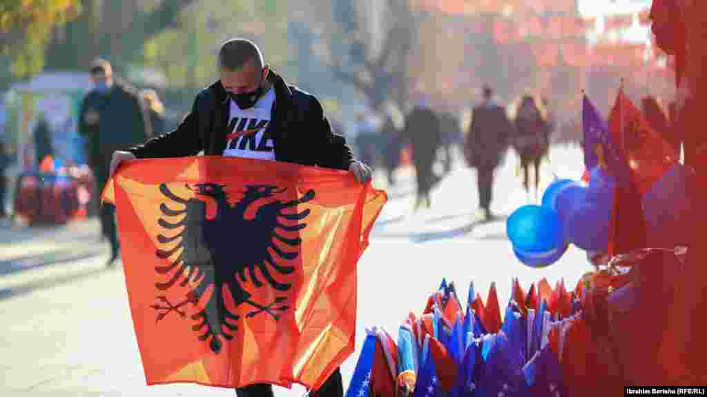 Një shitës mban në duar një flamur kuq e zi në sheshin “Nëna Terezë” në Prishtinë.