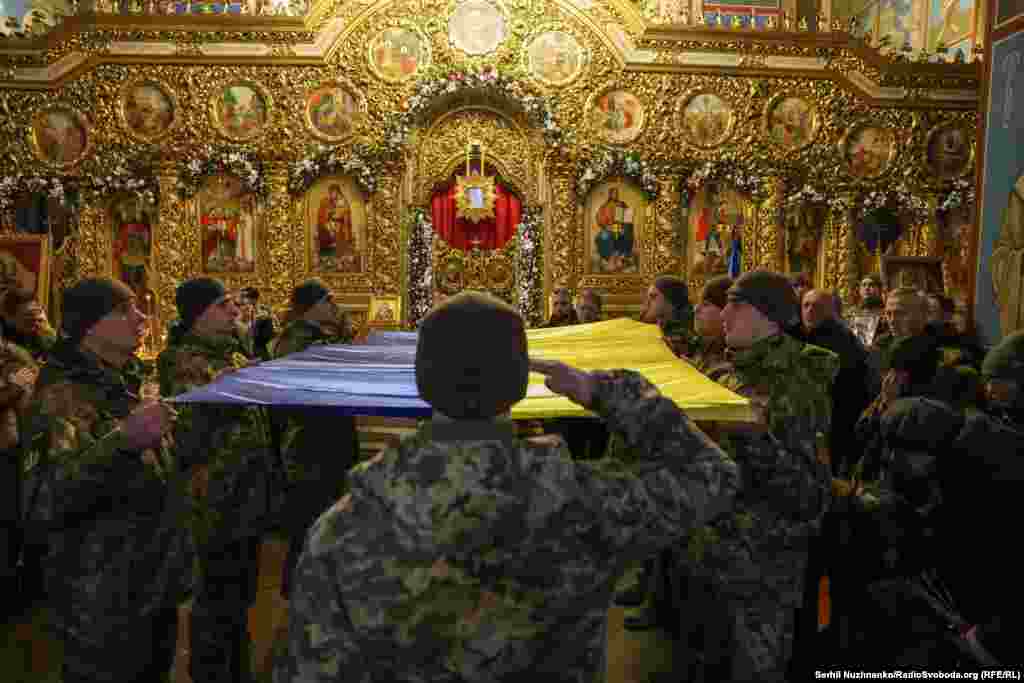 Побратими накривають труну українським прапором під час прощання у Михайлівському золотоверхому соборі. «Сьогодні мені вручили прапор, яким була накрита твоя труна. Сьогодні всі кидали в твою могилу землю, а я поклала в неї своє серце. Люблю тебе. Ми тебе любимо. І любитимемо завжди», – написала у своїй сторінці у фейсбуці дружина загиблого військового Анастасія Федченко
