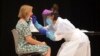Një punëtore shëndetësore duke testuar një grua për koronavirus.