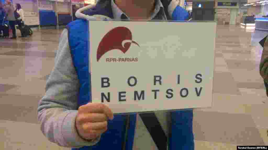 «Борис Немцов» деген жазу ұстаған белсенді Ресейден келген жолаушыларды қарсы алатын жерде тұр. Прага, 2 сәуір 2015 жыл.
