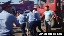 Полиция қызметкерлері орталық базар алдында сауда орнын бұзуға қарсылық танытқан әйелді әкетіп барады. Шымкент, 30 шілде 2018 жыл.