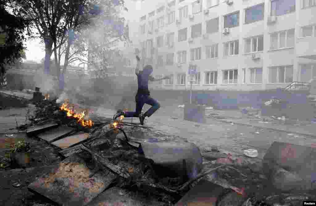 Un bărbat mascat sare peste o baricadă în flăcări în centrul orașului Mariupol pe 9 mai 2014. La începutul lunii mai, au început să se audă împușcături sporadice. În centrul orașului domnea fărădelegea, iar loialitatea în rândul forțelor de ordine locale părea incertă. 