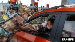 Ухань қаласындағы шлагбаумда сақшылар жүргізушінің дене қызуын өлшеп жатыр. 23 қаңтар 2020 жыл.