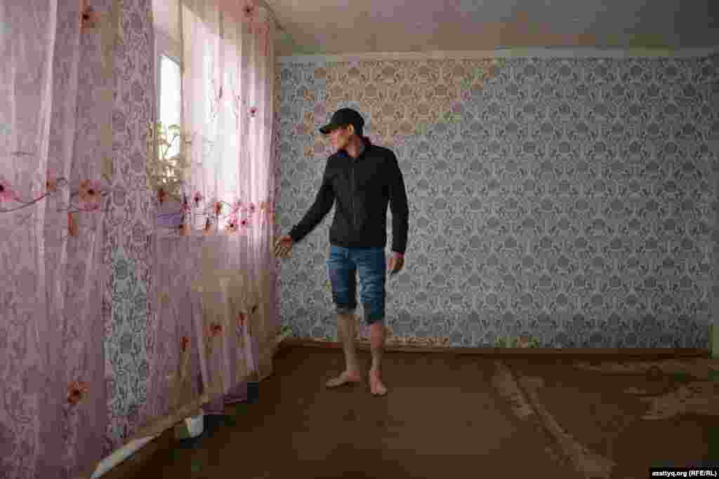 Су алған үйін көрсетіп тұрған Махамбет тұрғыны. Қабырғадағы дым белдеуінен жайылған судың деңгейін аңғаруға болады. Тұруға жарамсыз болып қалғандықтан, мұндағы үйлердің көбі қаңырап бос тұр. 