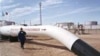 Рабочий на фоне нефтепровода, поставляющего нефть с месторождения Тенгиз.